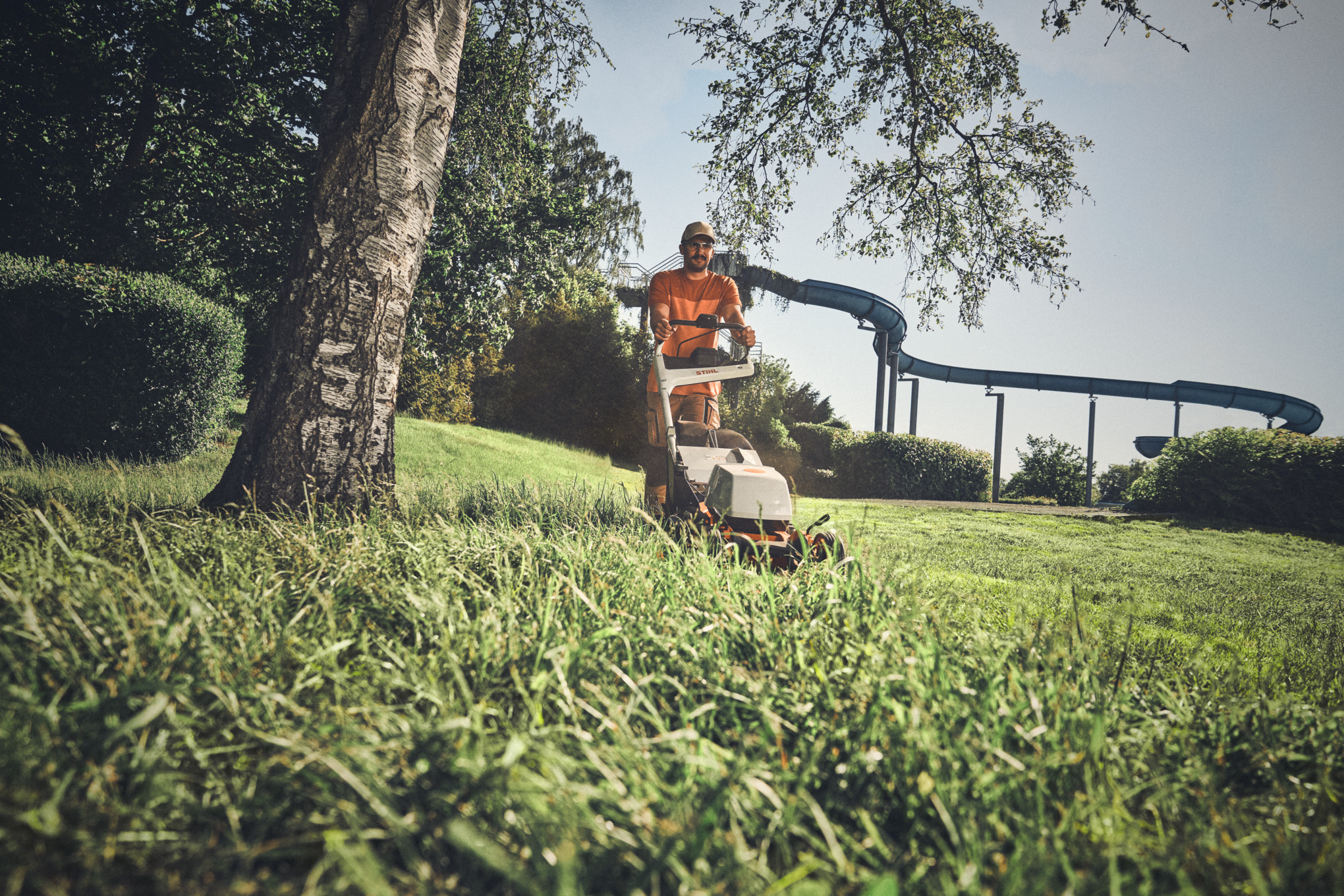 Uomo che cammina in giardino di fianco ad una siepe con un tosasiepi STIHL in mano.