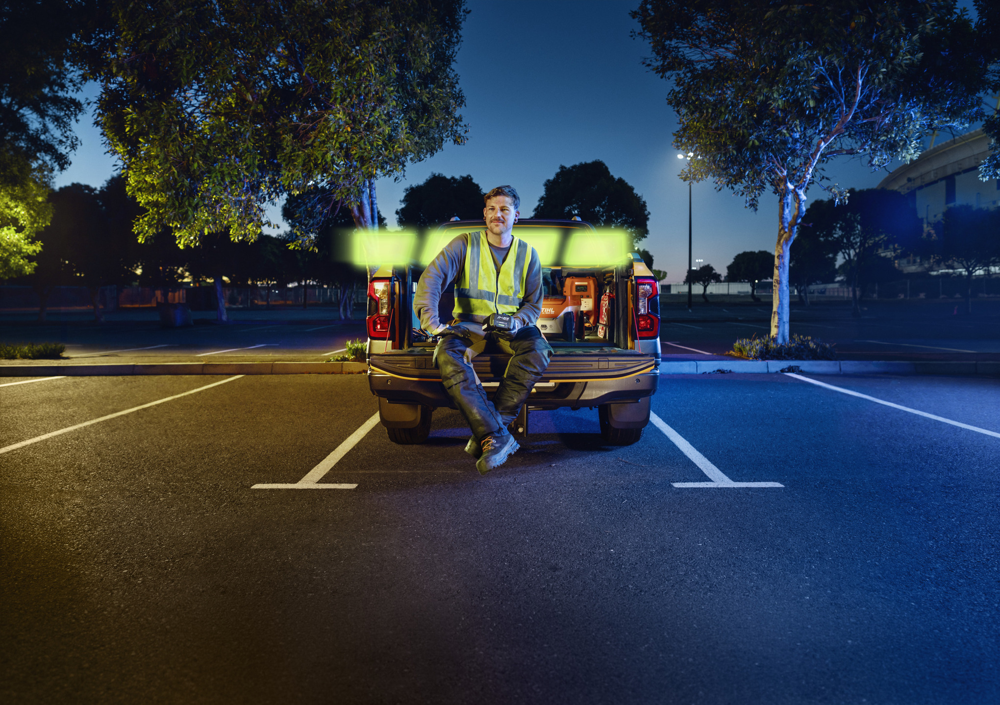  Professionista del verde seduto sul pianale di un pick-up che tiene in mano una batteria STIHL AP 300.0 P C ALLPRO