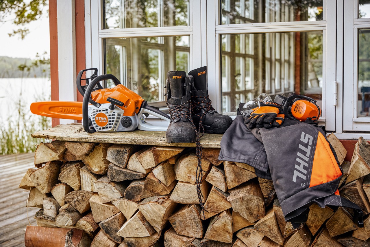 Indumenti protettivi STIHL e il prodotto MS 162 su uno scaffale sopra la legna accatastata