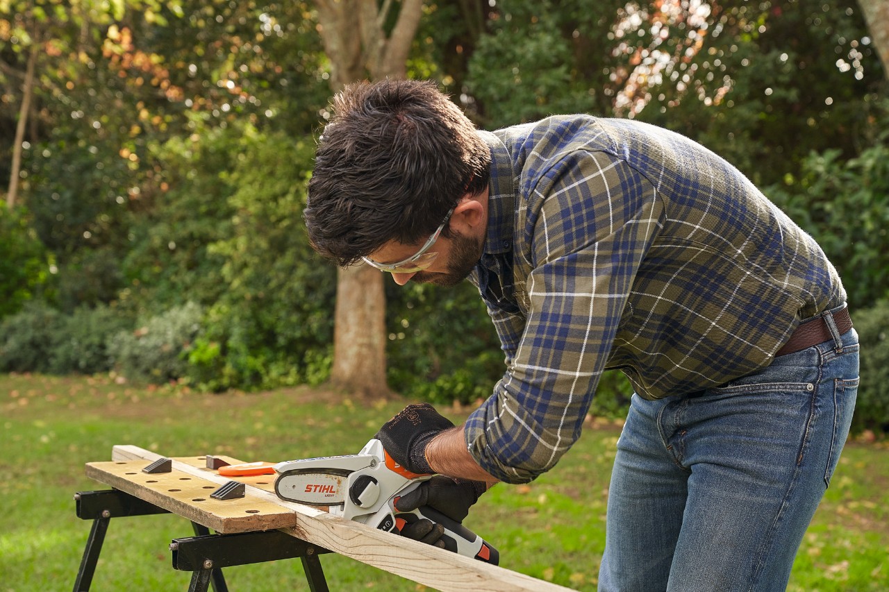 Un uomo con occhiali di sicurezza e guanti protettivi STIHL taglia un listello di legno con il potatore a batteria STIHL GTA 26