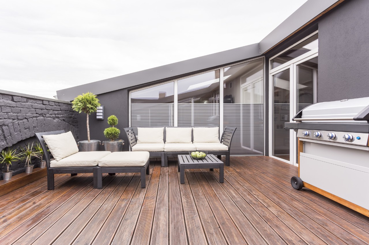 Mobili da giardino, barbecue e piante su una terrazza sul tetto con pavimentazione in legno
